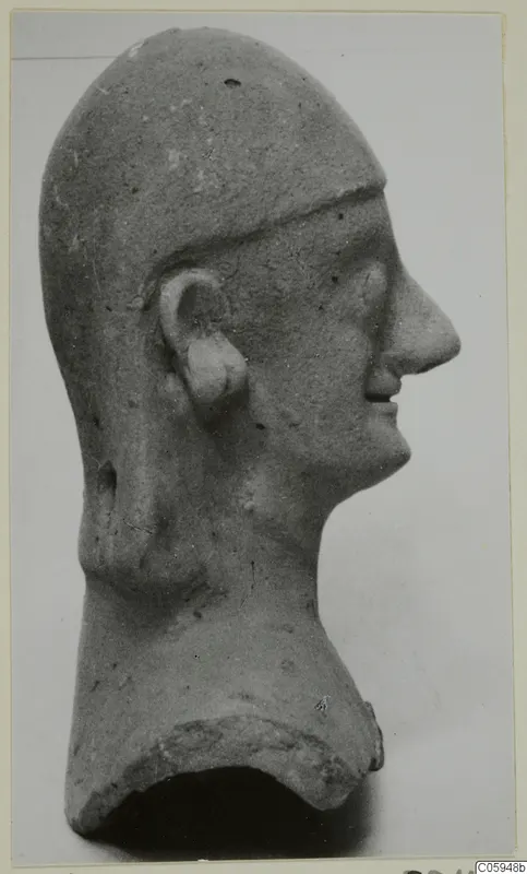 Terracotta head fragment in right profile, with a cap-like covering over the crown and a broken neck