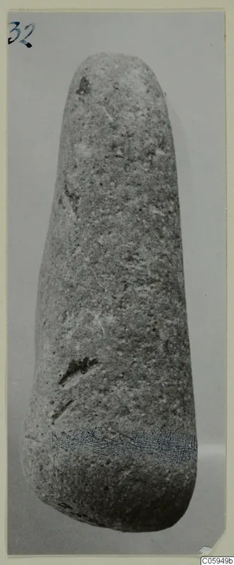 Elongated stone object with a rounded top and wider base, photographed upright on a grey backdrop.