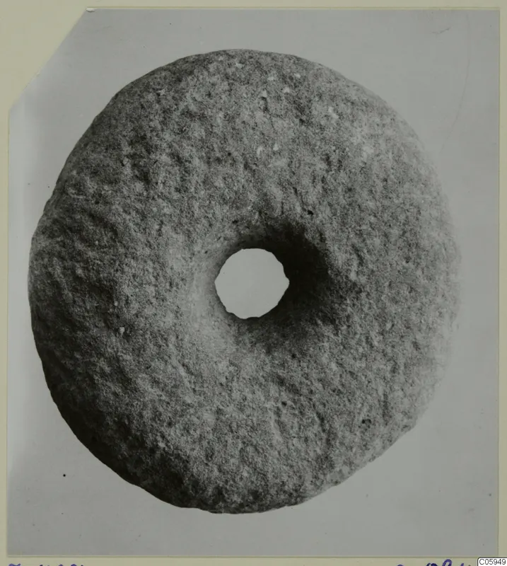 Round stone disc with a central hole, photographed from above on a grey backdrop