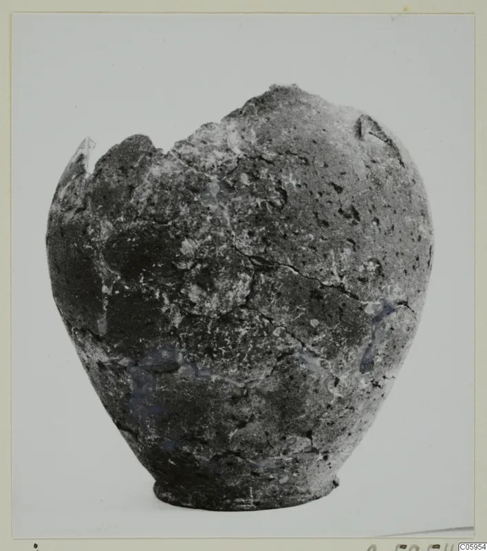 Hand-made coarse pottery vessel with a broken rim, photographed against a plain light background