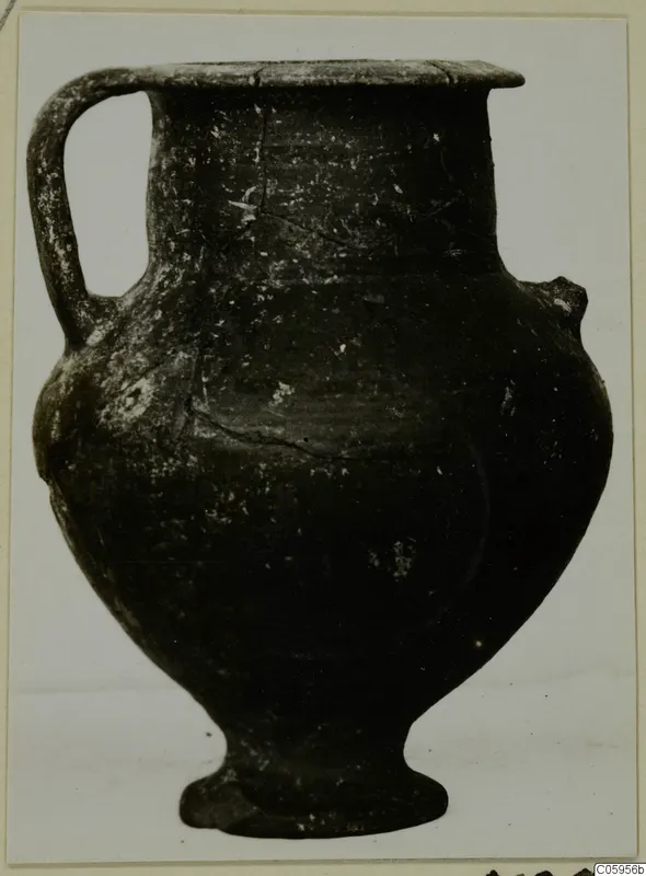 Pottery Black-on-Red vessel with a single handle, a flared rim and a footed base, shown against a pale background.