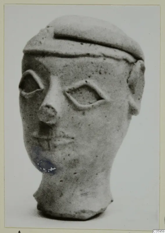 Terracotta head figurine from Ayia Irini with a flat cap-like top and almond-shaped eyes, shown against a plain background
