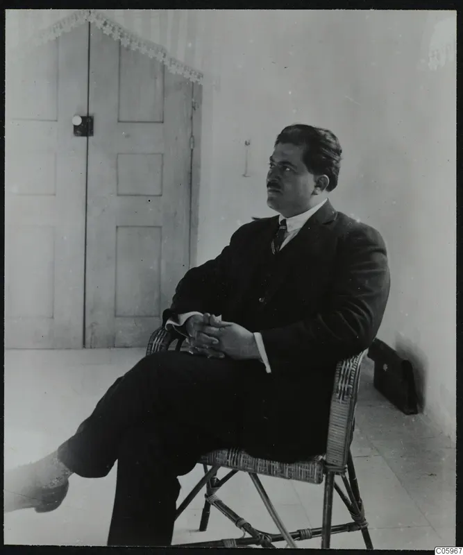 Mr. Kaplanis, mayor of Lapithos, seated in a wicker chair in front of a panelled door