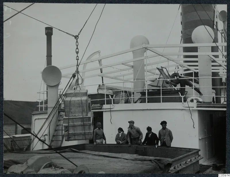 Wooden crates swinging on a chain from a cable on the deck of M/S Gotland at Famagusta, with men and a woman watching.