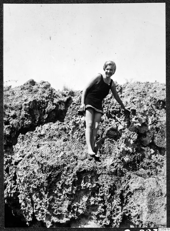 Gudrun Atterman perched on rough, eroded rock in a dark swimsuit, smiling at the camera