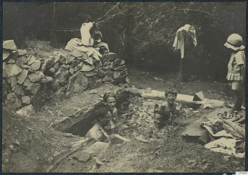 Four people bathing in a stone-lined cistern at Machairas while a child in a hat watches from the edge.