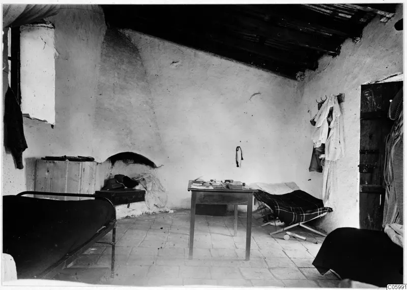 Interior of a whitewashed room at Machairas with two metal beds, a wooden table and a built-in fireplace