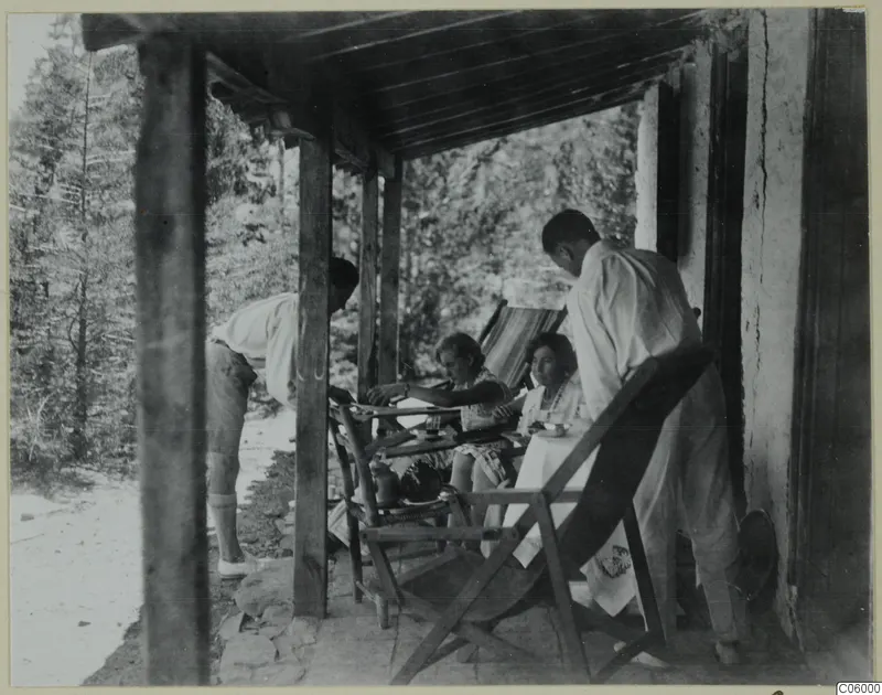 Four people eating on a timber-posted terrace outside a whitewashed house at Machairas, with pine trees behind.