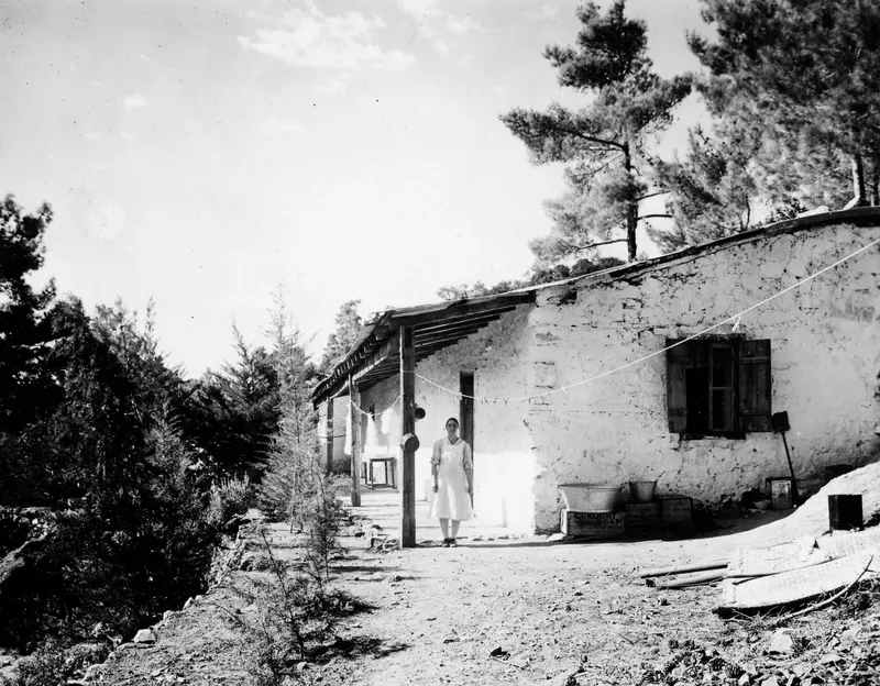 House at Machairas with a woman standing by its doorway, washing hung on a line along the verandah