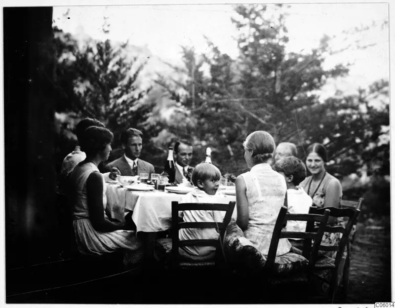 People seated at a table laid for a meal on an outdoor terrace under trees at Machairas.