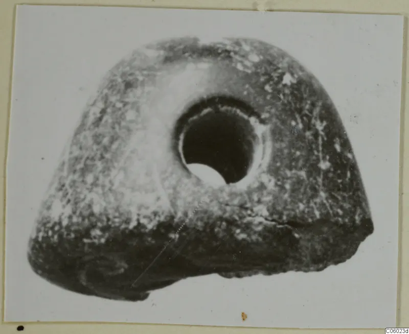 Pierced stone object with a large round hole through its upper centre, shown on a mounted print