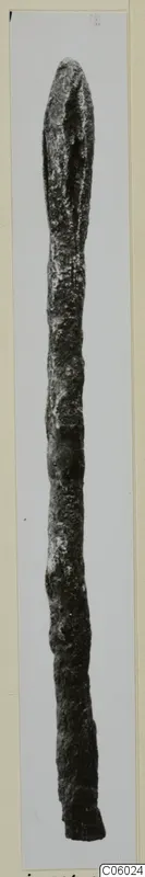 Long slender bronze object, a fragment with a pointed upper end, photographed on a light background.