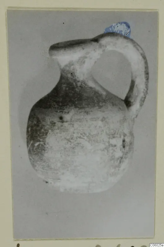 Small jug with a strap handle and a wide spout, photographed against a grey background on a card mount