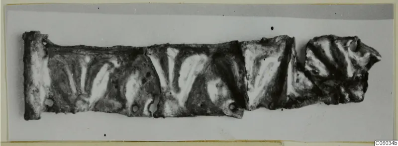Fragmentary silver strip with raised chevron pattern, made of several joined pieces, lying flat on a pale ground