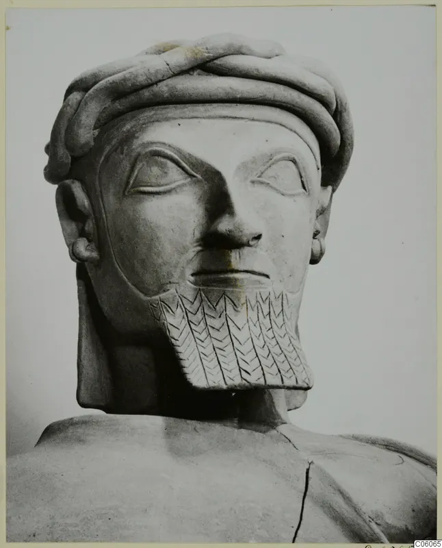 Head and shoulders of a bearded male statue with a twisted headband and a chevron-incised beard
