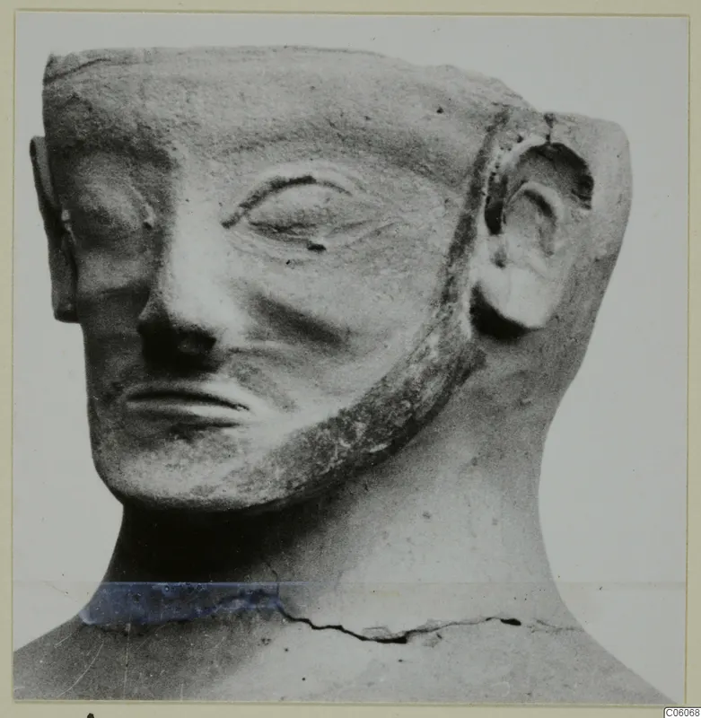 Terracotta Proto-Cypriote I statuette: head with a flat-topped headdress, beard along the jaw and large ear, seen in three-quarter view.