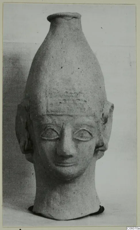 Terracotta head-shaped vessel with a tall neck rising from the crown, Ayia Irini, photographed against a plain background