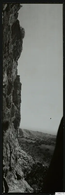 Steep rock cliff with a path climbing its face, with a valley of trees and hills beyond, at Fylleri near Kythrea