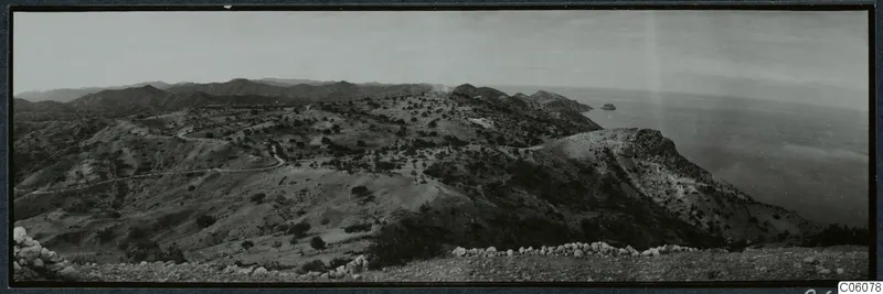 Panoramic view over hilly land with a winding track and the sea on the right, seen from Vouni.