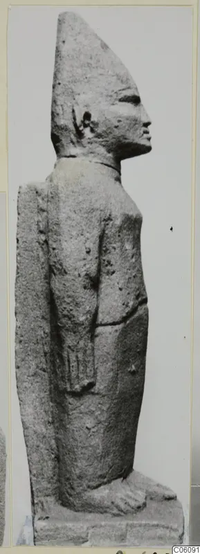 Limestone Cypro-Egyptian statue of a standing figure in side profile, wearing a tall pointed headdress.
