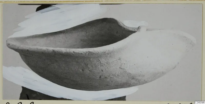 Terracotta lamp, an open boat-shaped clay vessel with a pointed end, photographed against a grey backdrop