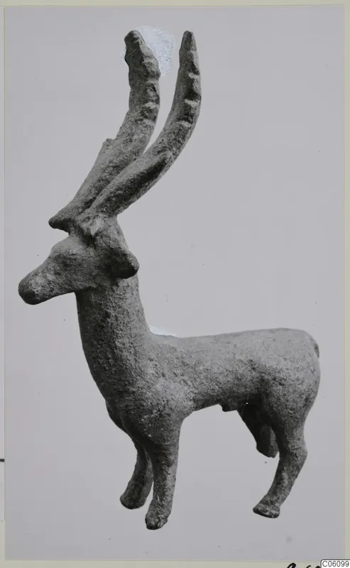 Bronze figurine of a standing animal with two long, ridged horns, shown in side view