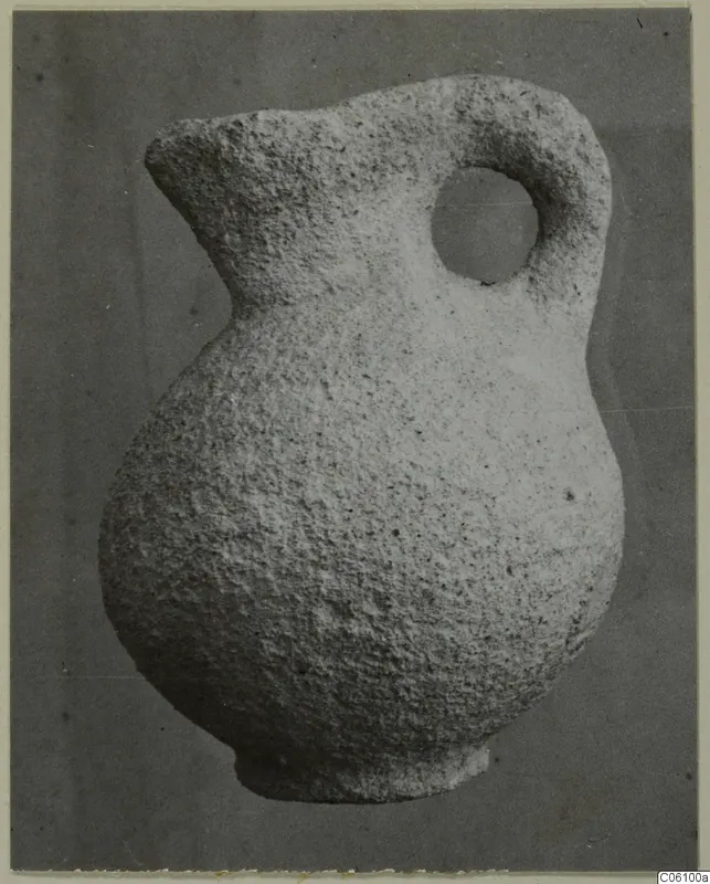 Small stone jug with a rounded body, a spout and a single loop handle, photographed against a grey background