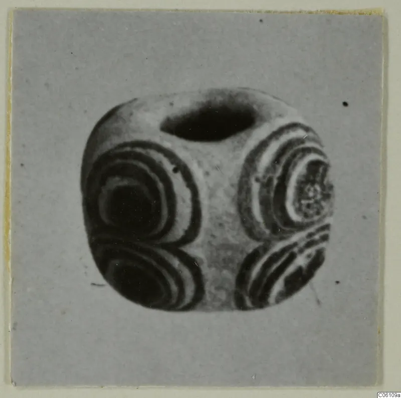 Bead with concentric banded rings on several faces and a large hole through the top, shown on a grey card.