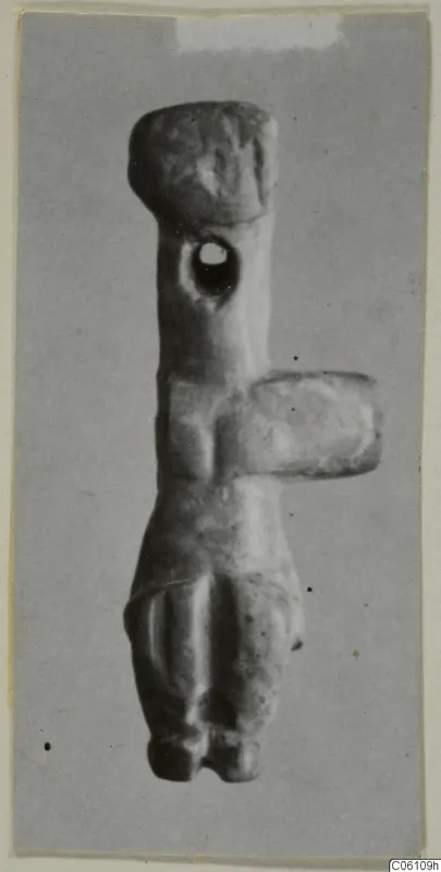 Stone idol with a rounded head, a hole pierced through the upper body and a side projection, photographed on grey card