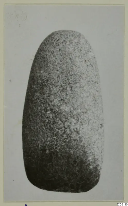 Small stone object with a rounded top and broader base, shown against a plain grey background