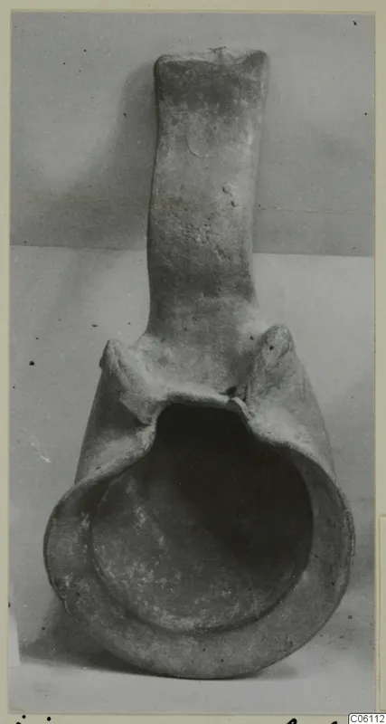 Terracotta lamp with a tall handle and a broad open bowl, photographed against a plain grey backdrop