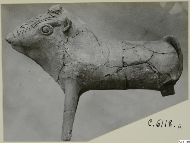 Terracotta animal figure in side view, with incised zigzag lines on the head and a long projecting stub below the body