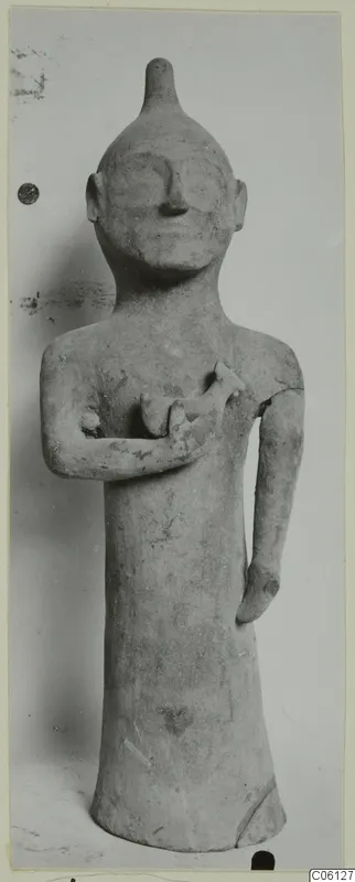 Terracotta statuette of a standing figure with a pointed head, one arm bent across the chest holding a small object.