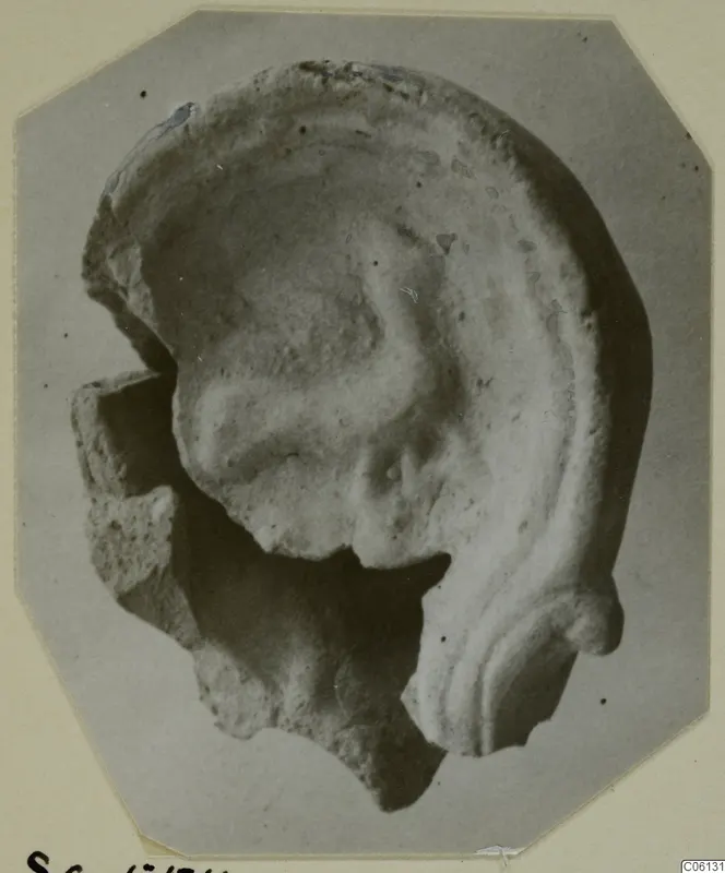 Fragment of a terracotta lamp with a raised curved rim and broken edges, photographed on a grey card mount.