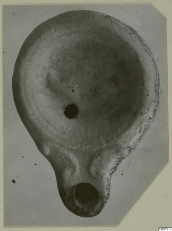 Terracotta oil lamp seen from above, with a filling hole and a round nozzle at the lower end.