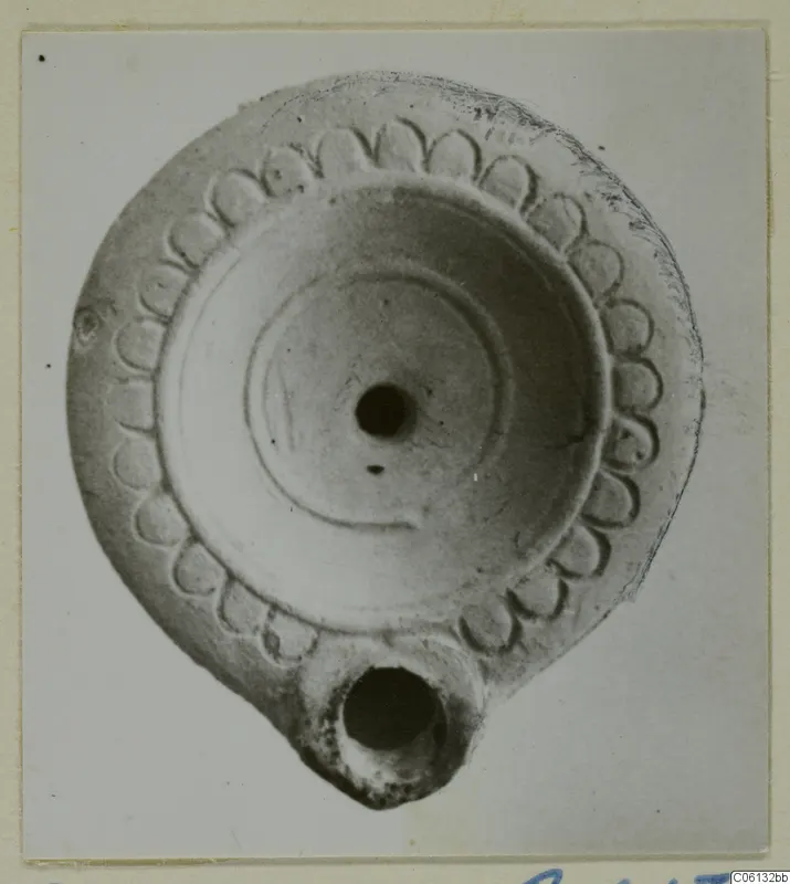 Terracotta oil lamp seen from above, with a ring of leaf-like petals around the rim and a filling hole.