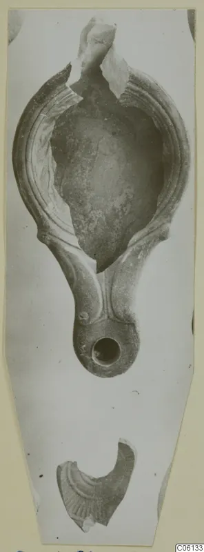 Terracotta oil lamp with a broken nozzle, shown from above, with a loose fragment below.