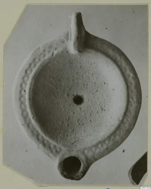 Terracotta oil lamp with a upright handle and a round filling hole, seen from above.