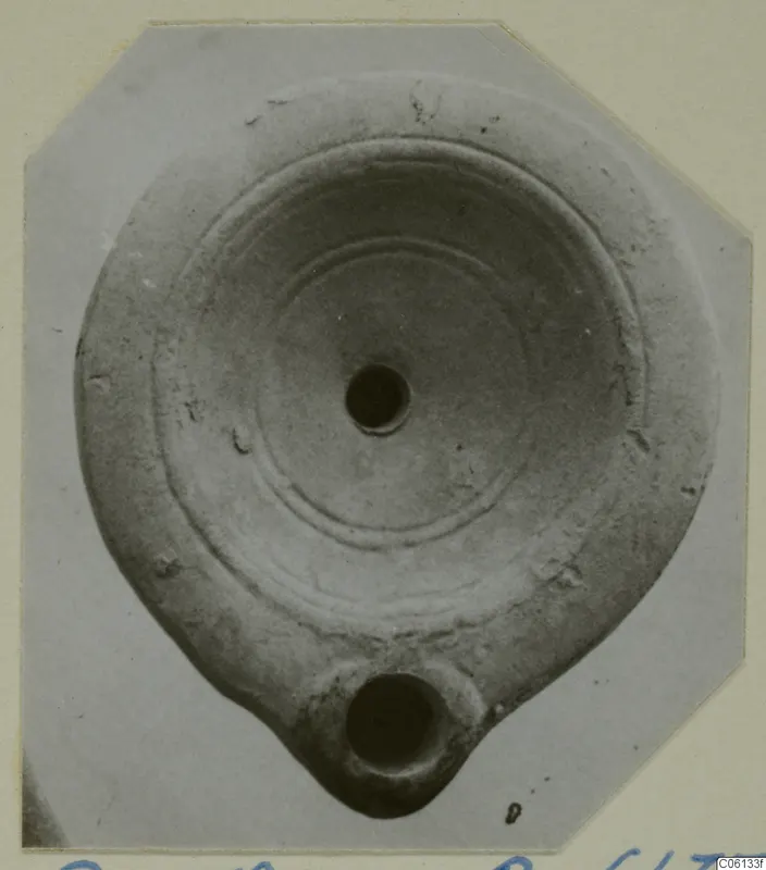 Terracotta lamp seen from above, with concentric rings on its disc and a nozzle with a round opening at the bottom.