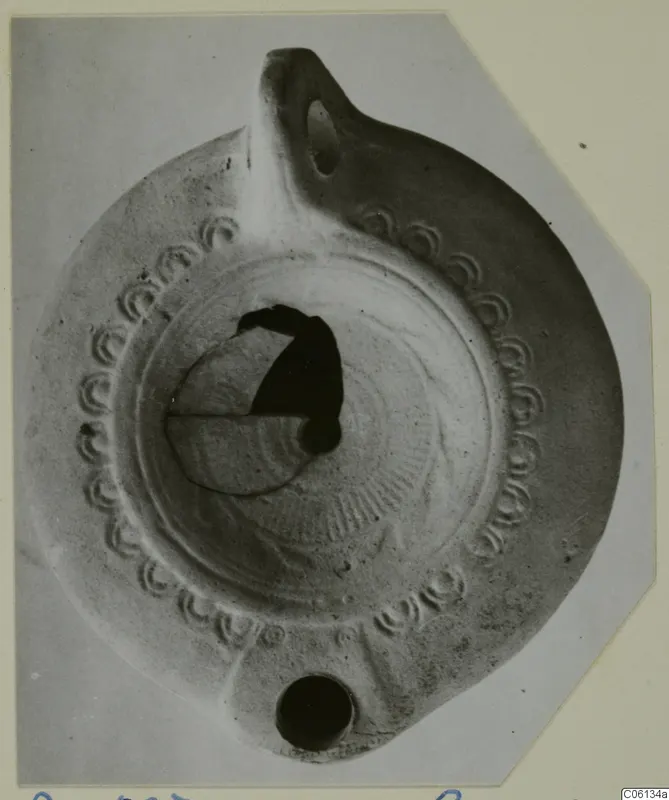 Terracotta oil lamp with a row of impressed arcs around the rim and a handle at the top