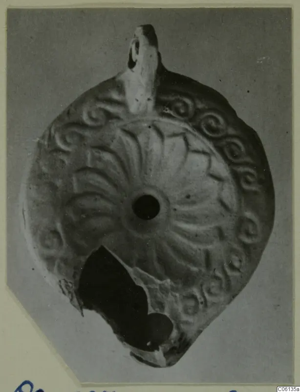 Terracotta oil lamp seen from above, with radiating leaf-like ribs and spiral motifs around the filling hole