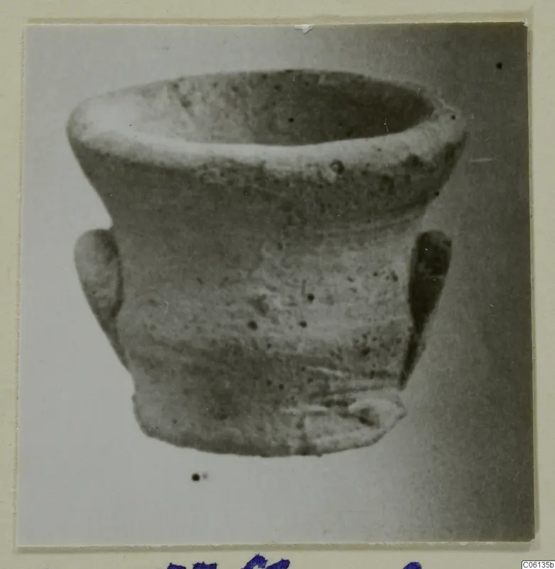 Small plain pottery cup with a rounded body, flared rim and two small handles, photographed on a light background.
