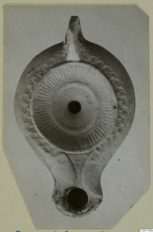 Terracotta oil lamp seen from above, with a radial ribbed disc, a pattern border and a nozzle at the top.