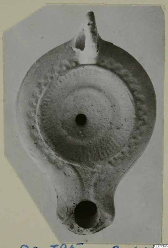 Terracotta oil lamp seen from above, with a nozzle at the top, a handle at the bottom and a central filling hole.