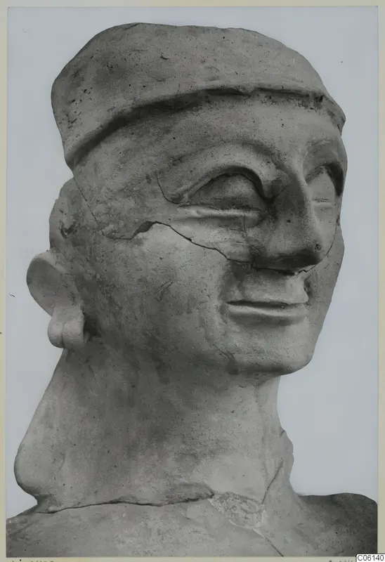 Bust of a figure with a flat cap-like headdress, large eyes and a cracked surface, seen in close view against a plain background