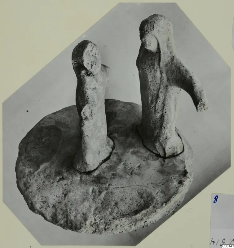 Two terracotta figurines standing on a shared circular base, photographed against a grey backdrop