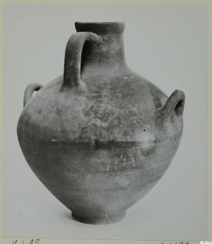Coarse pottery jar with a narrow neck and three handles, from Idalion, photographed against a grey backdrop