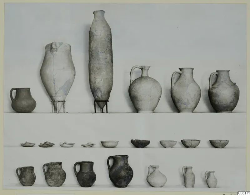 Pottery from Vouni Tomb 2 in three rows: handled jugs, two large vessels, and bowls against a plain backdrop.