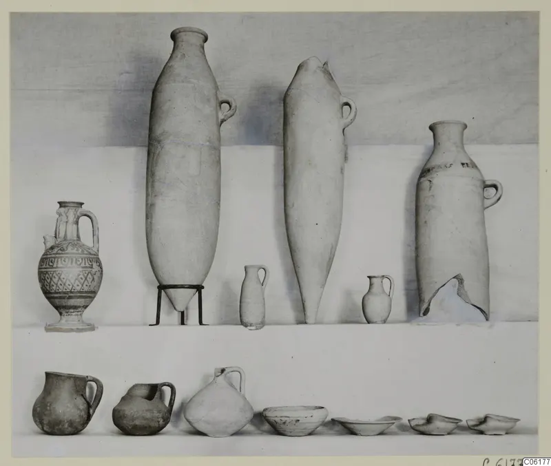 Pottery vessels from Tomb 16 at Vouni: jars, jugs and bowls set out in two rows against a pale backdrop.