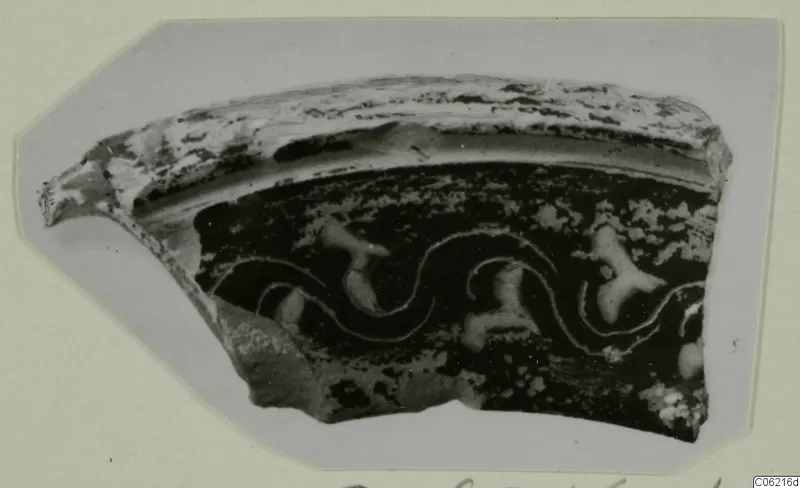 Fragment of a pottery vessel wall with a curved rim, dark surface and pale wavy lines and blobs